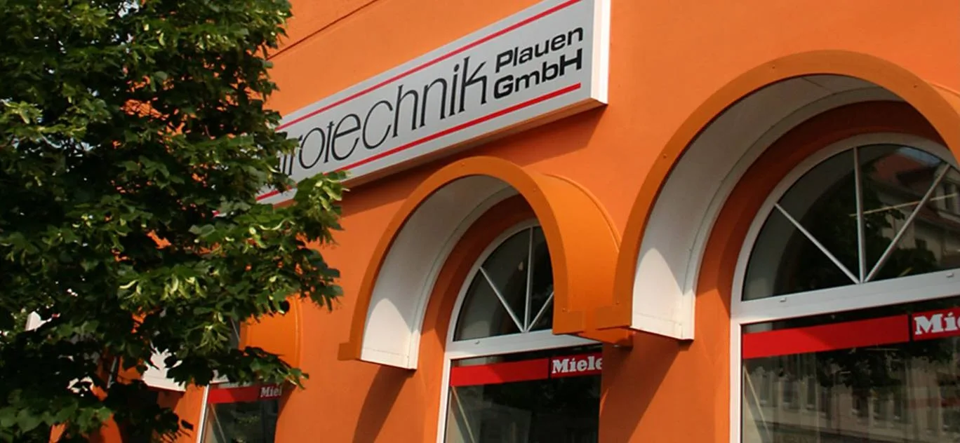 Orange Fassade mit dem Firmenschild elektrotechnik Plauen GmbH und Rundbogenfenstern