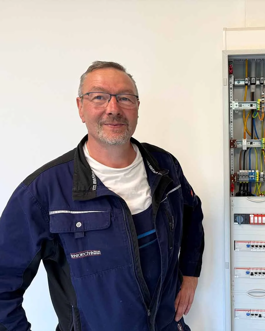 Mann in Firmenjacke mit dem Logo der elektrotechnik Plauen vor einem fertig verdrahteten Verteilerschrank